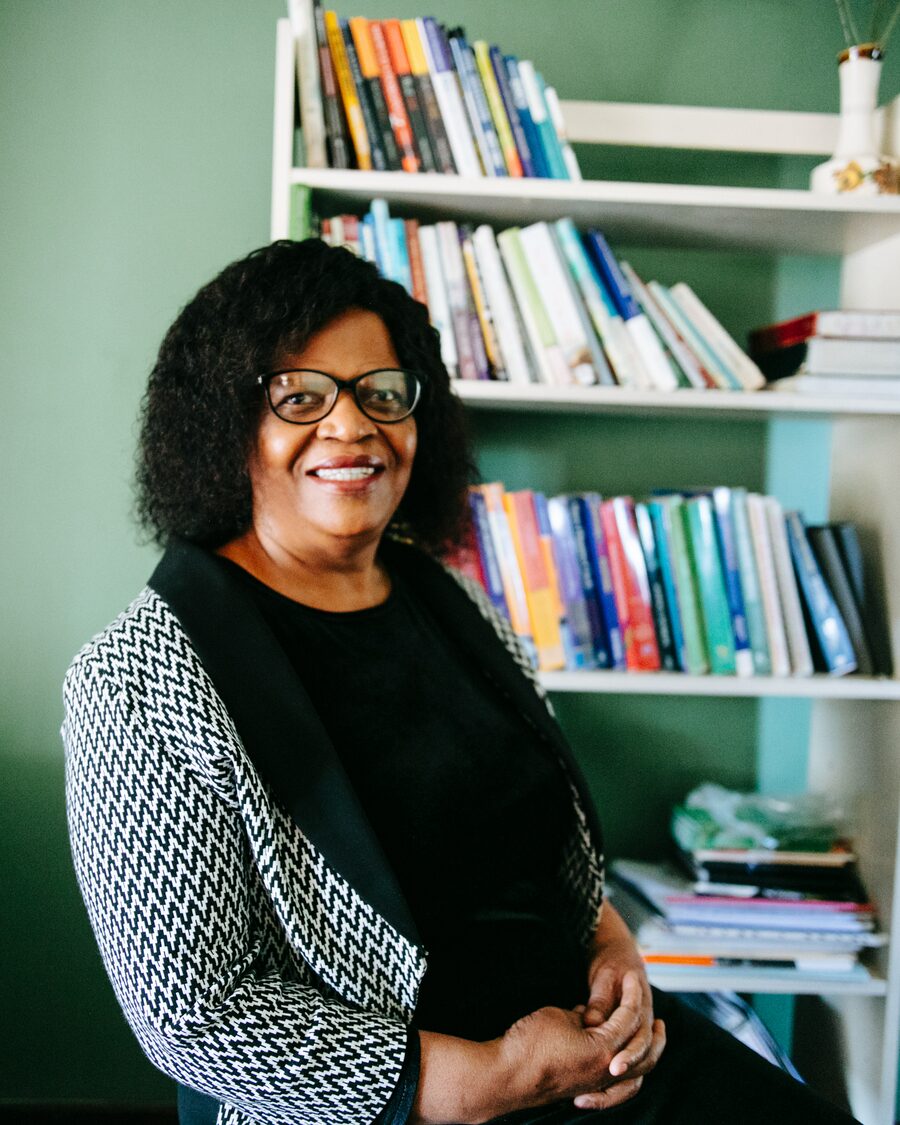 Coach Thato smiling beside her bookshelf