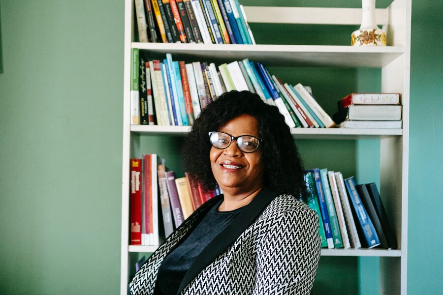 Coach Thato seated and smiling in front of her bookshelf